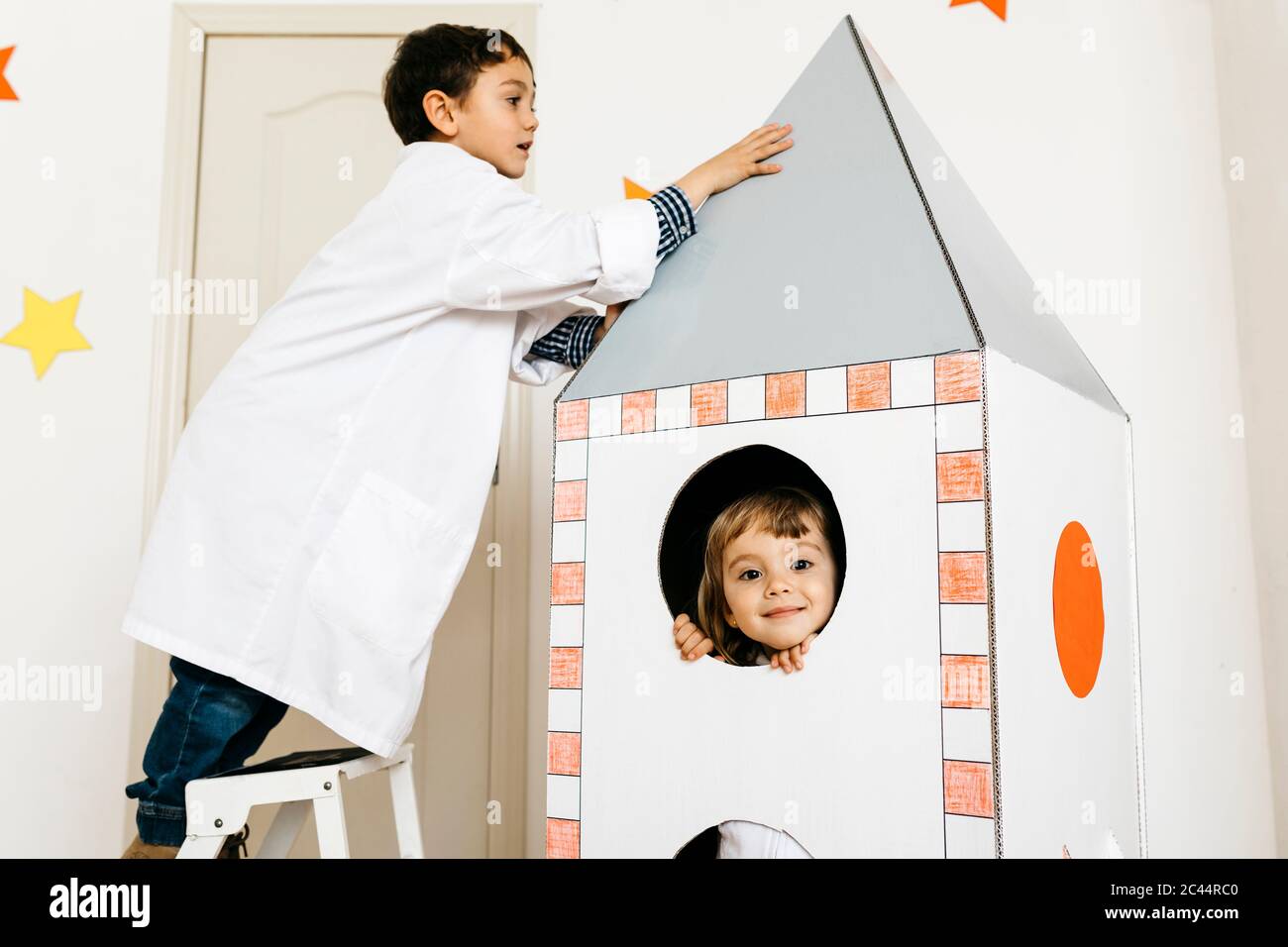 Siblings playing astronaut and researcher at rocket Stock Photo