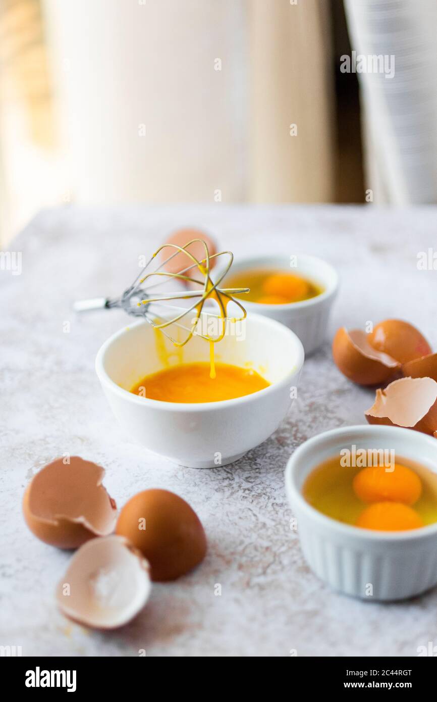 Wire whisk, eggshells and bowls with egg yolks Stock Photo