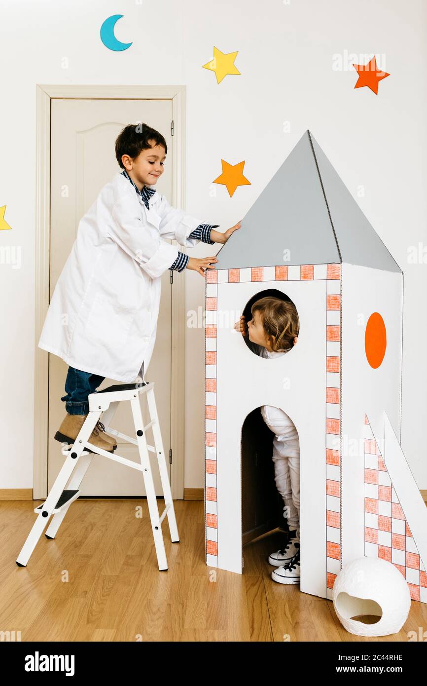 Siblings playing astronaut and researcher at rocket Stock Photo