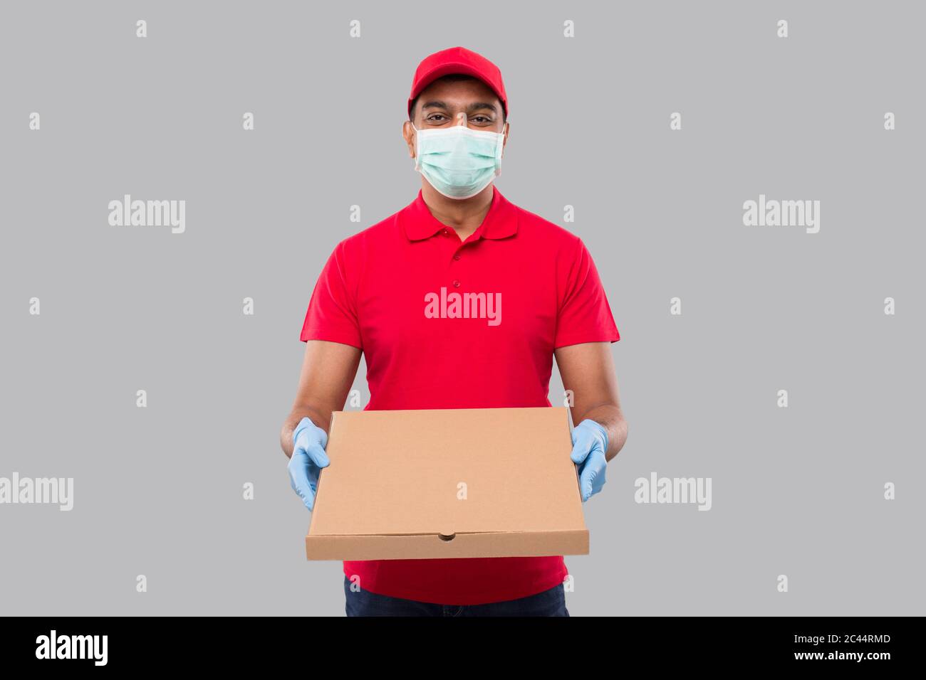 Delivery Man Pizza Box in Hands Wearing Medical Mask and Gloves Isolated. Red Tshirt Indian Delivery Boy. Stock Photo