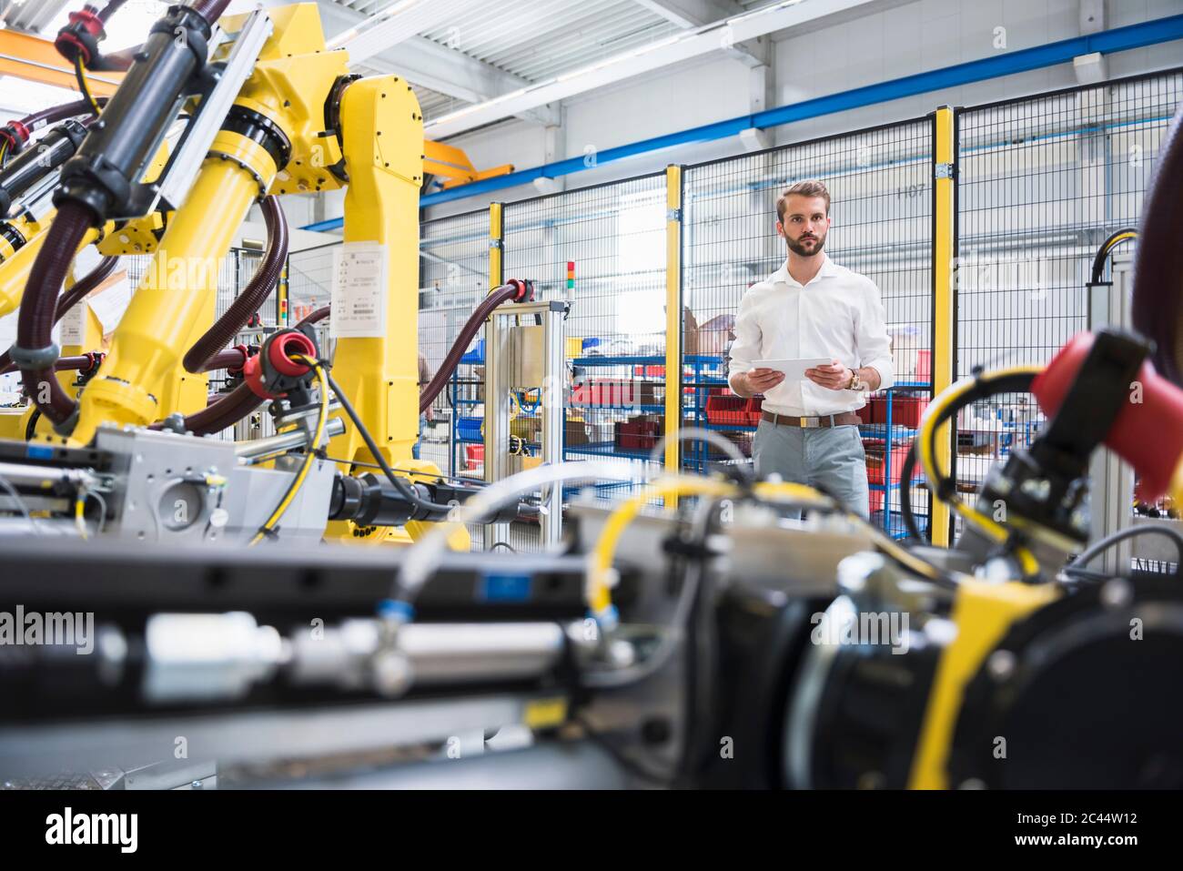Male robotics expert standing by computer-aided manufacturing technology at factory Stock Photo