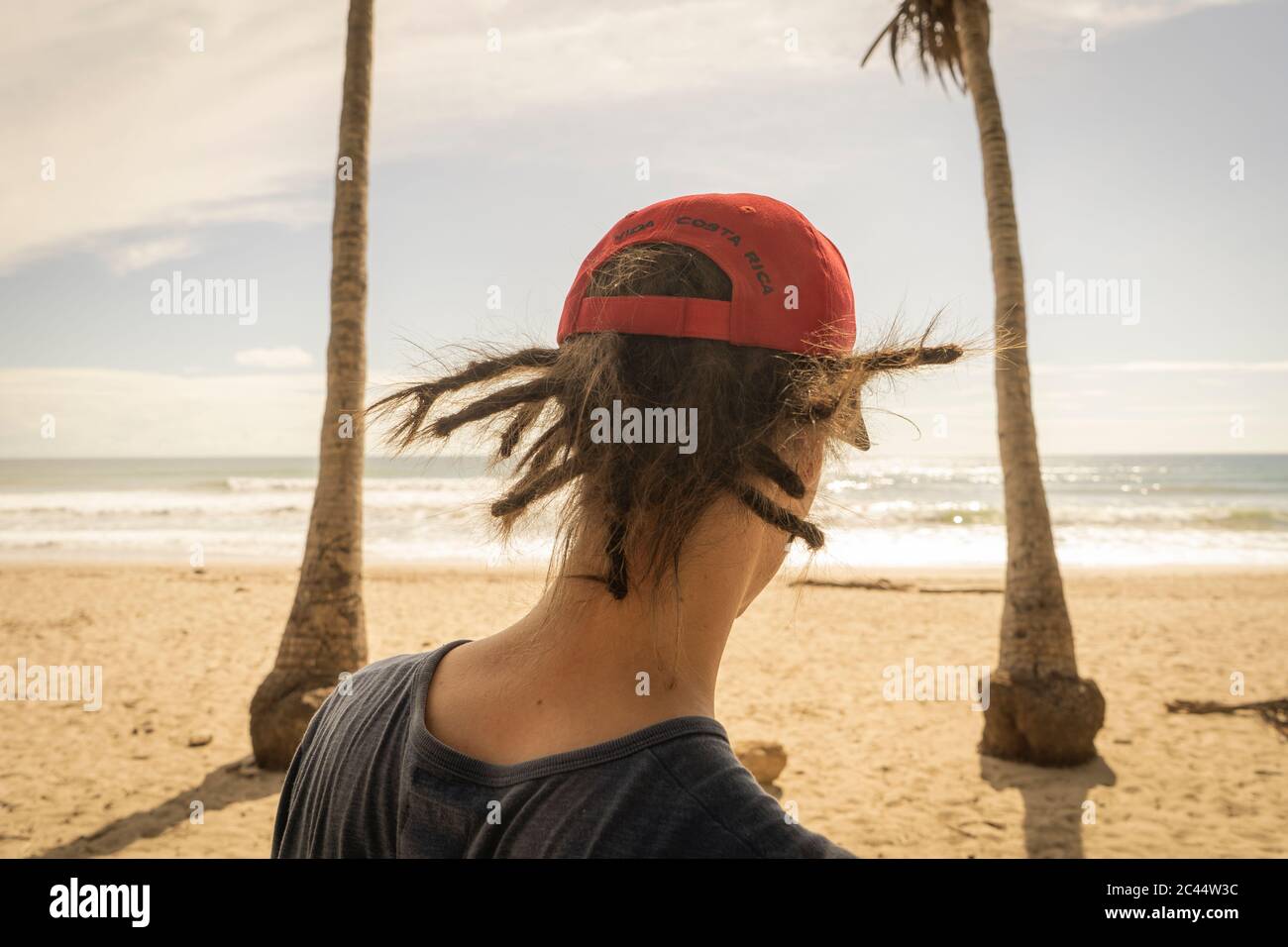 Costa Rica, Puntarenas Province, Puntarenas, Rear view of young man wearing dreadlocks looking at ocean from Playa Santa Teresa Stock Photo