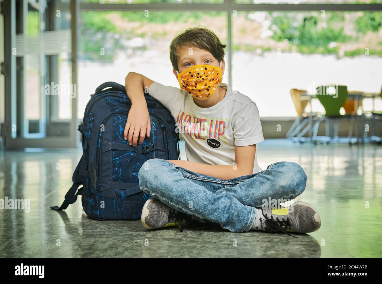 Boy sitting on the floor in school wearing mask Stock Photo