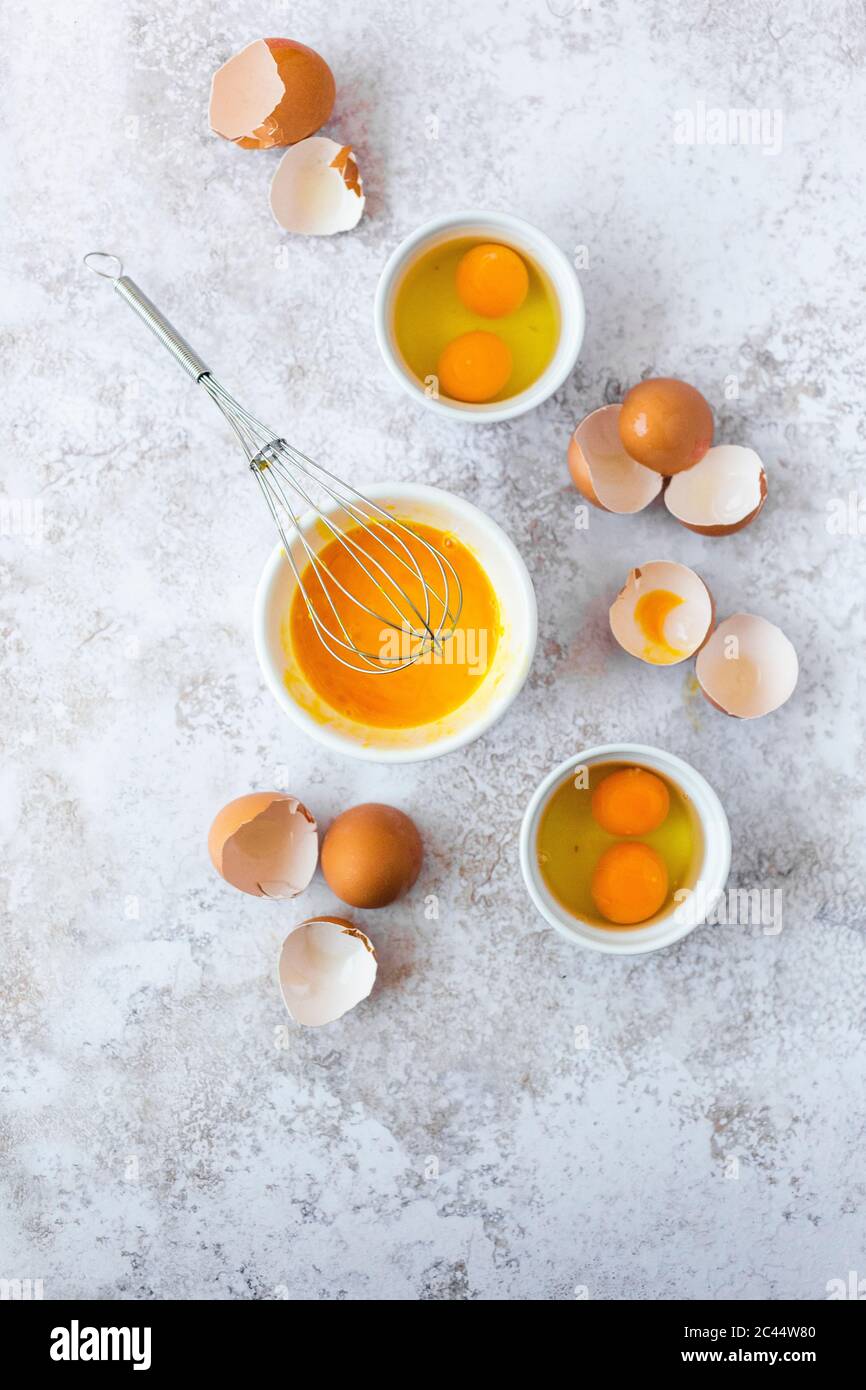 Wire whisk, eggshells and bowls with egg yolks Stock Photo