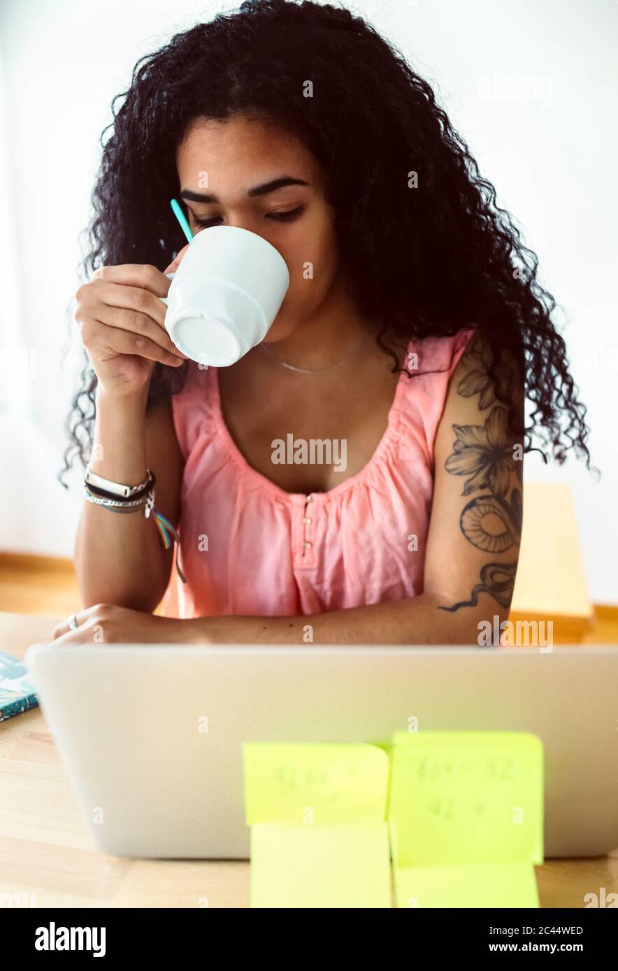 Young woman working from home using laptop and drinking coffee Stock Photo