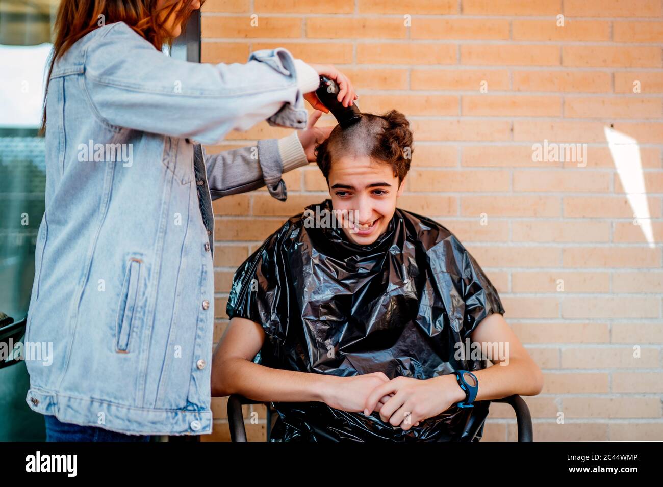 Mother shaving teenage son's head with electric razor against brick wall at  home Stock Photo - Alamy