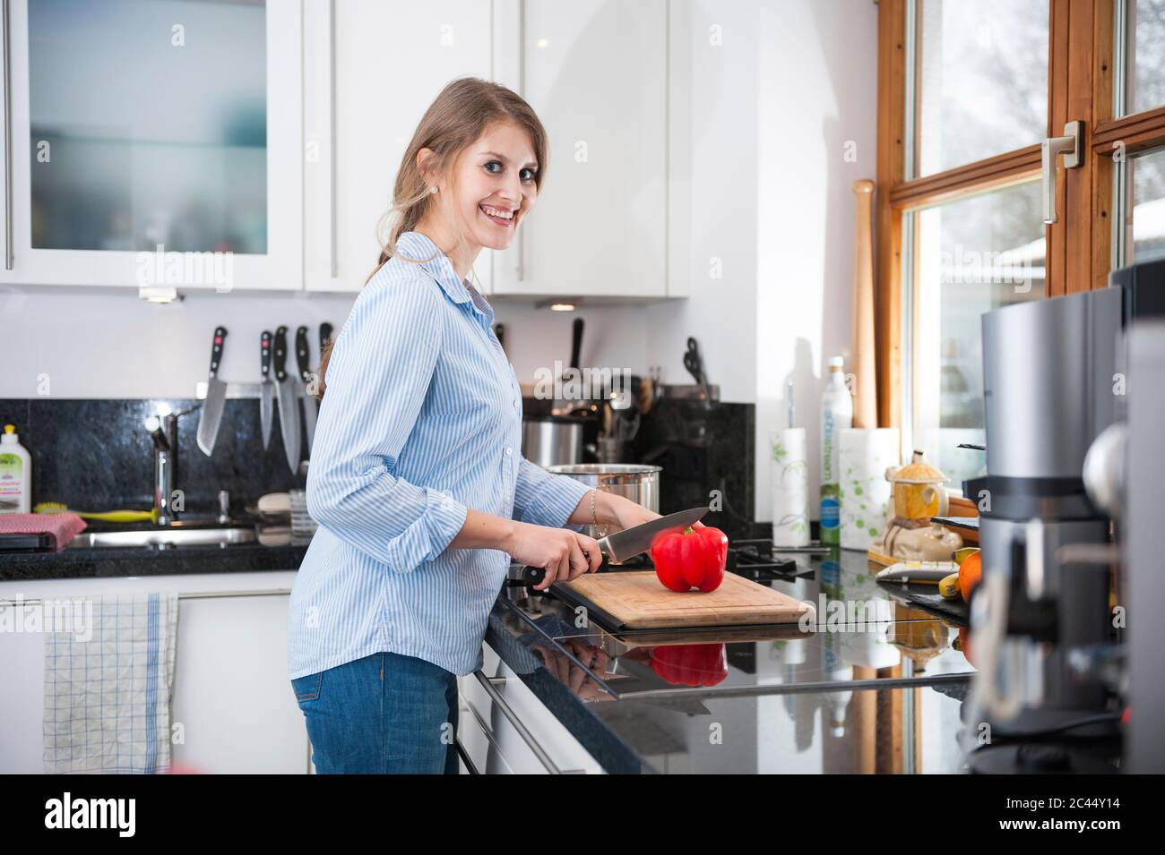 Smiling beautiful woman cutting red bell pepper at kitchen counter Stock Photo