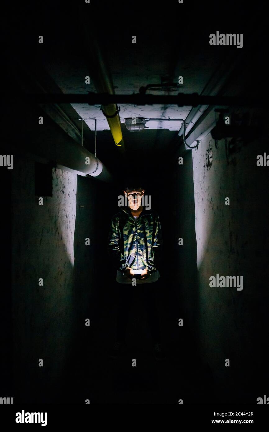 Man holding illuminated smart phone in dark corridor amidst old walls Stock Photo