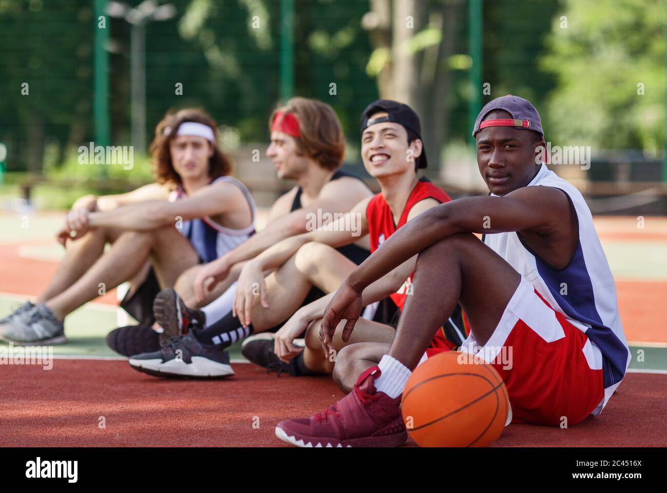 Multiracial team of basketball players getting some rest after their game at outdoor court, copy space Stock Photo