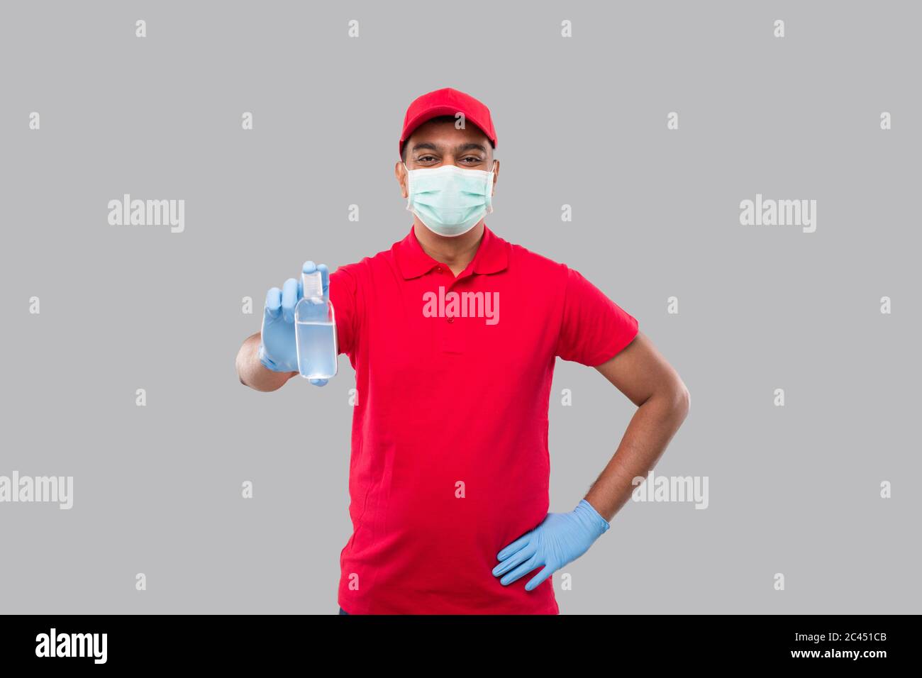 Delivery Man Showing Hands Sanitizer Wearing Medical Mask and Gloves Isolated. Indian Delivery Boy Holding Hand Antiseptic Stock Photo
