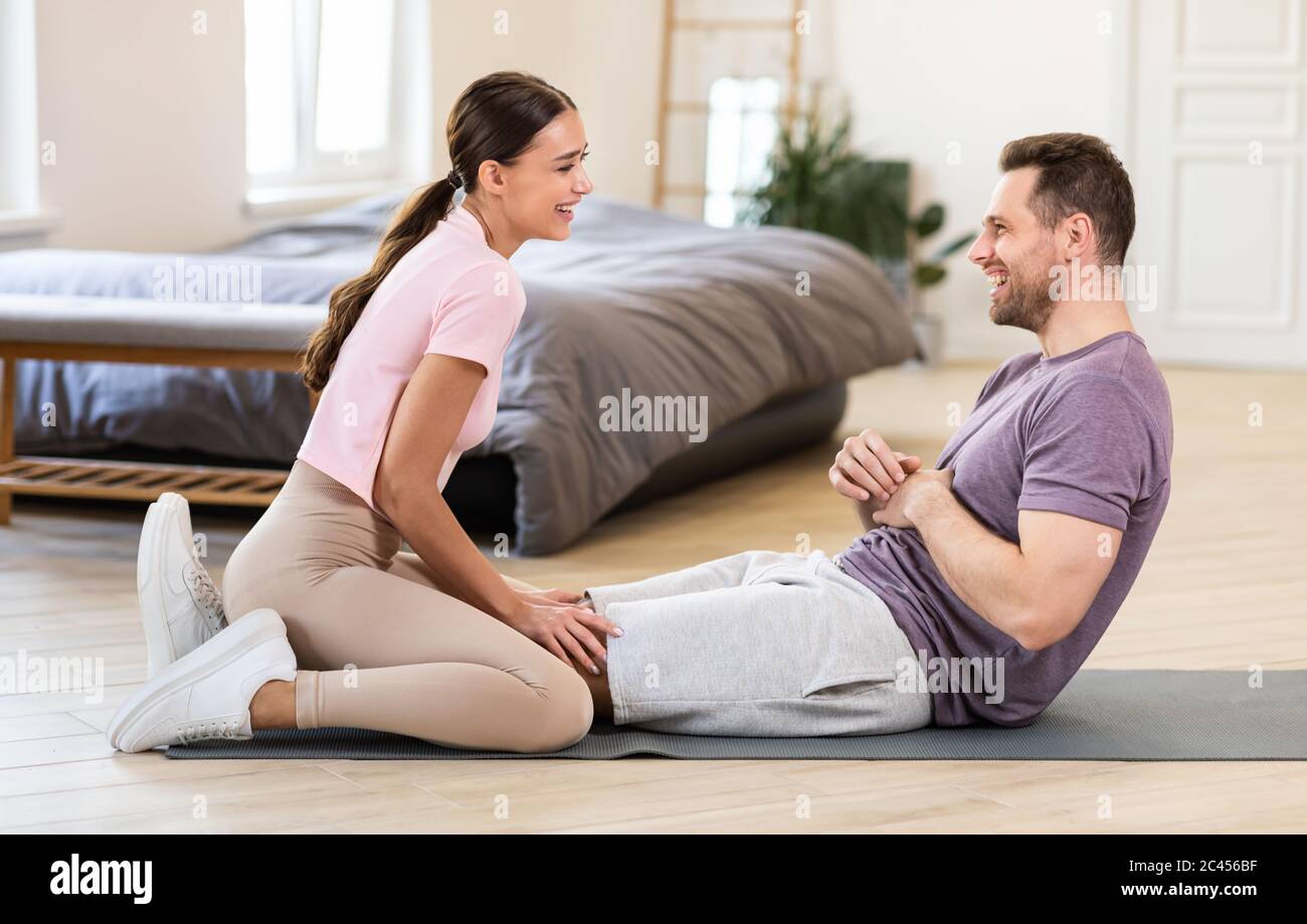 Girlfriend Sitting On Boyfriends Legs Helping Him Exercise At Home Stock Photo Alamy