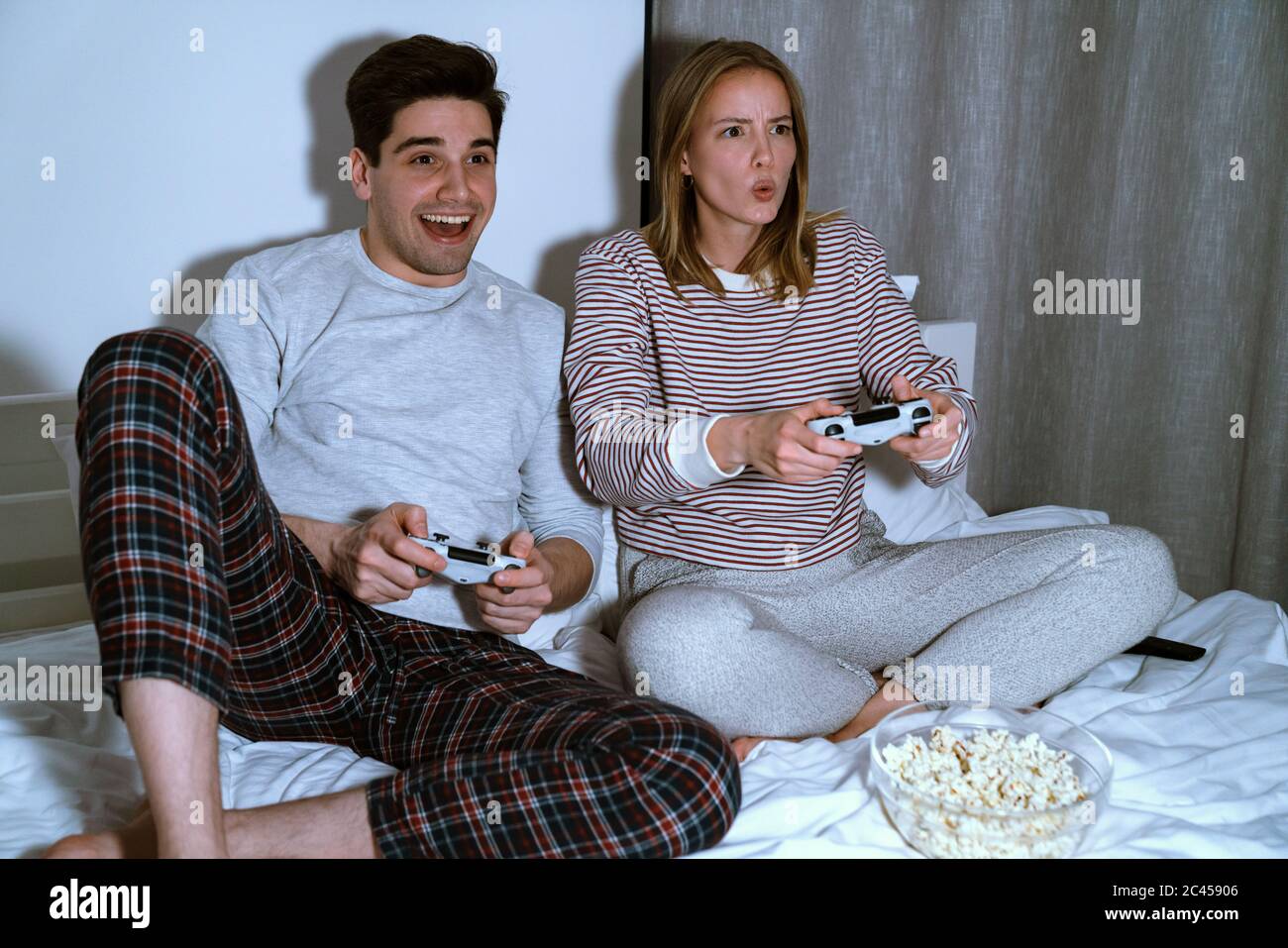 Portrait of excited cute couple holding joysticks while playing video games in bed at home Stock Photo