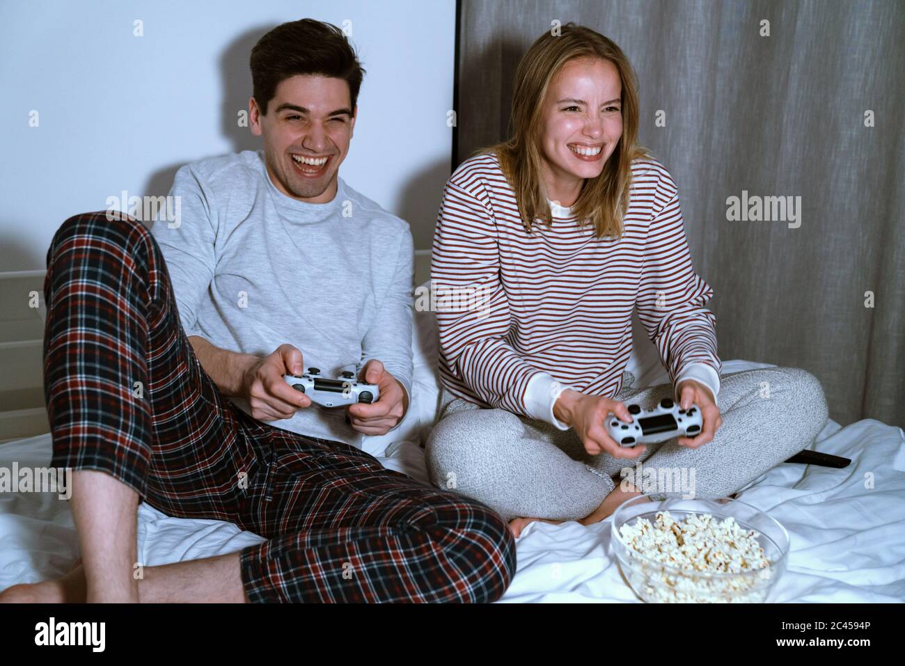 Portrait of excited cute couple holding joysticks while playing video games in bed at home Stock Photo
