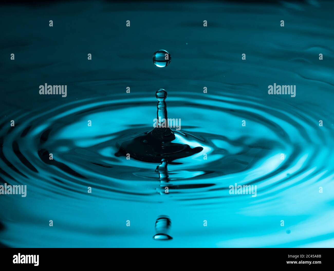 Perfect water drop splashing into smooth water causing ripples Stock