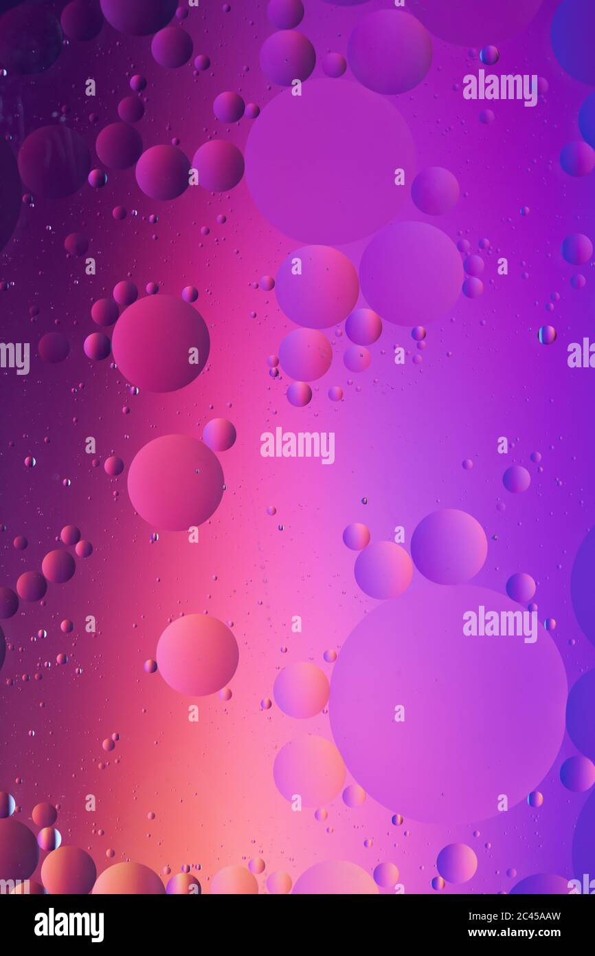 Macro photo of mixing oil and water. Oil droplets above a beautiful coloured abstract background creating circles and ovals. Stock Photo