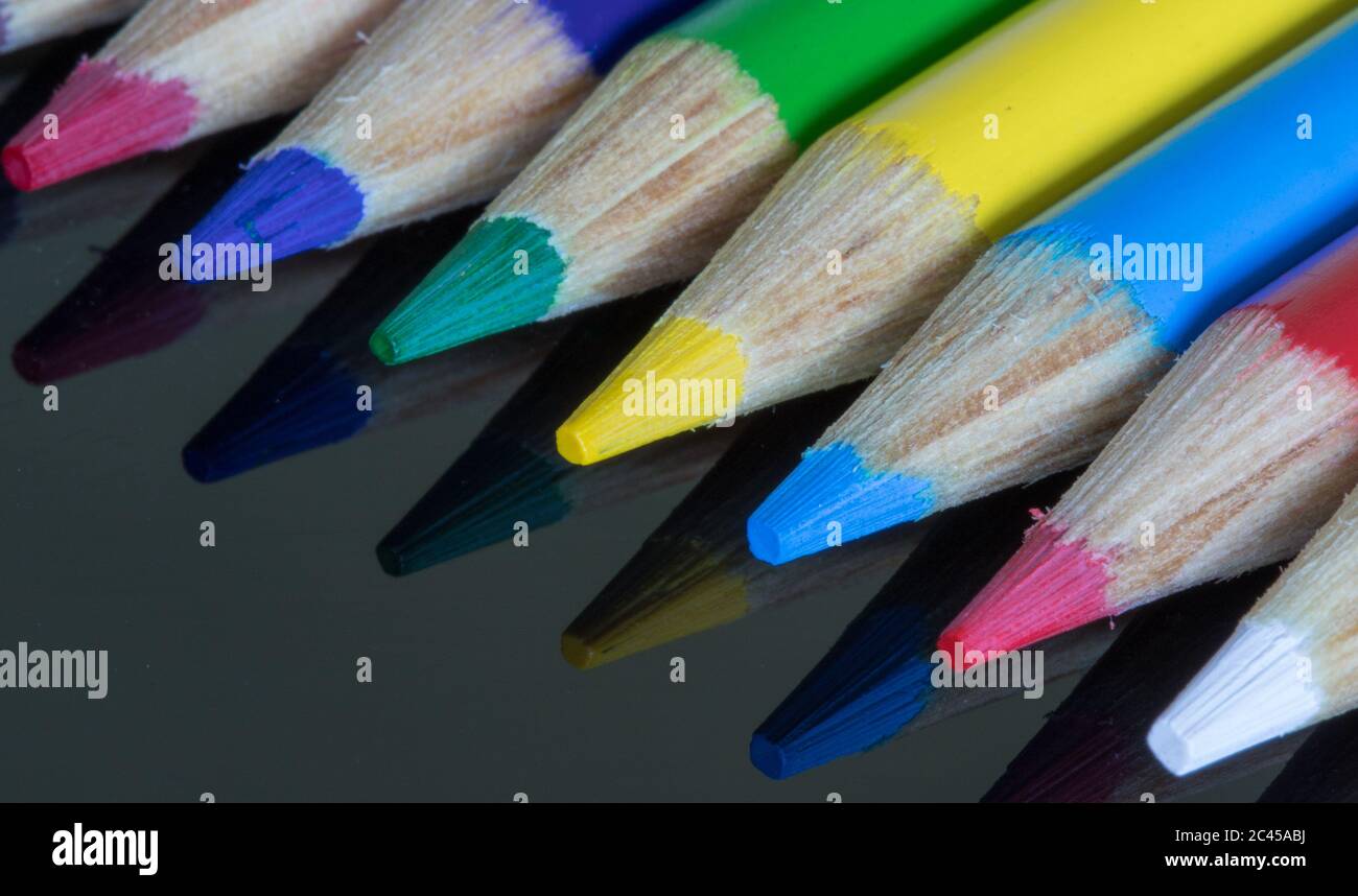 Coloured pencil crayons on a black reflective surface. Rainbow of