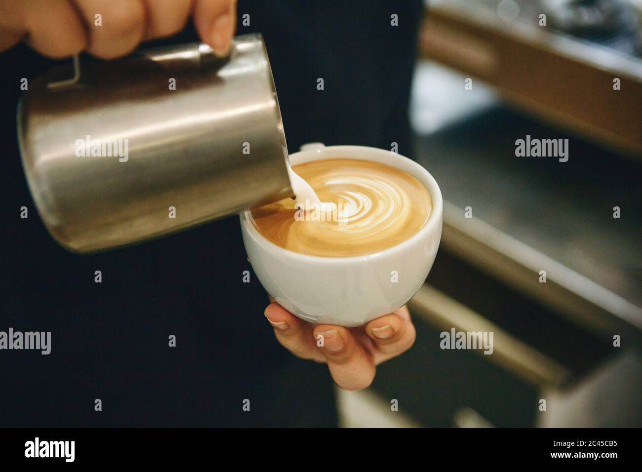 Barista pours milk or cream into coffee and draws a drawing on the foam