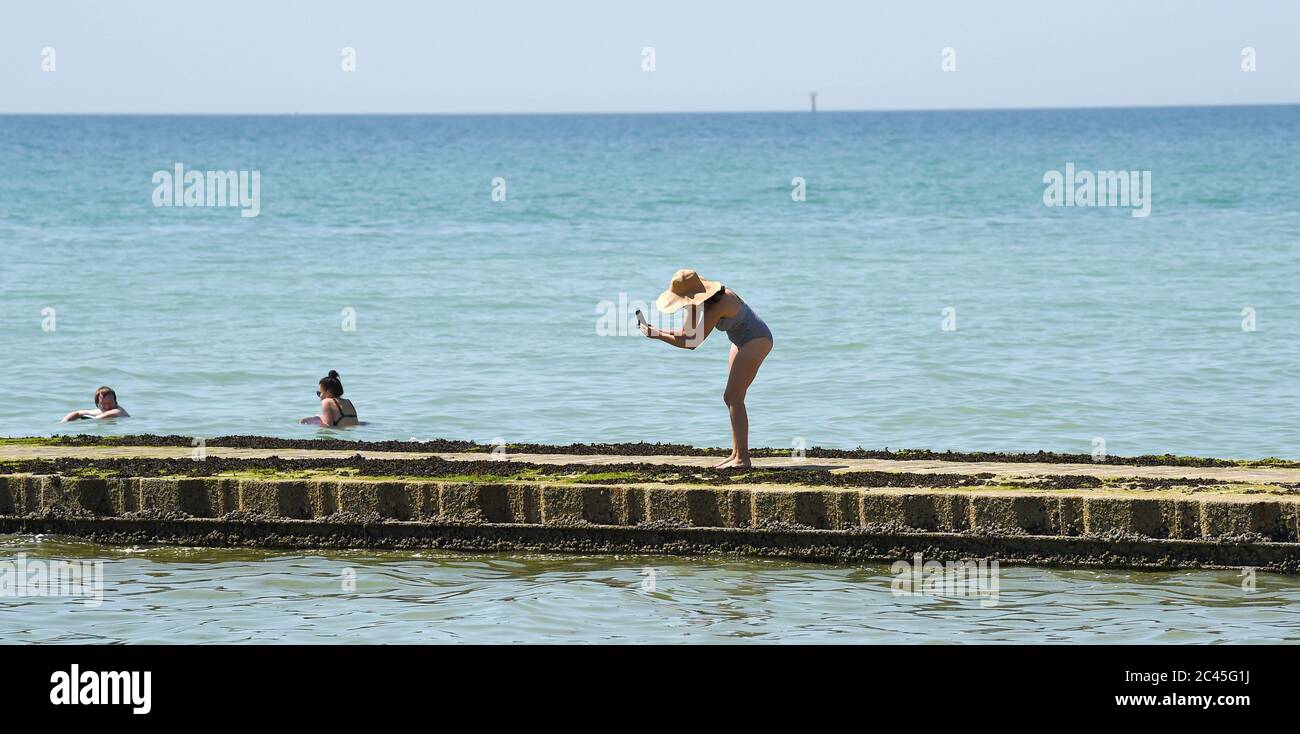 Worthing UK 24th June 2020 - A lady in a large sun hat takes some photographs as crowds hit the beaches at Ferring near Worthing in West Sussex today as they enjoy the heatwave weather  with temperatures reaching 30 degrees in some parts of the South East   : Credit Simon Dack / Alamy Live News Stock Photo