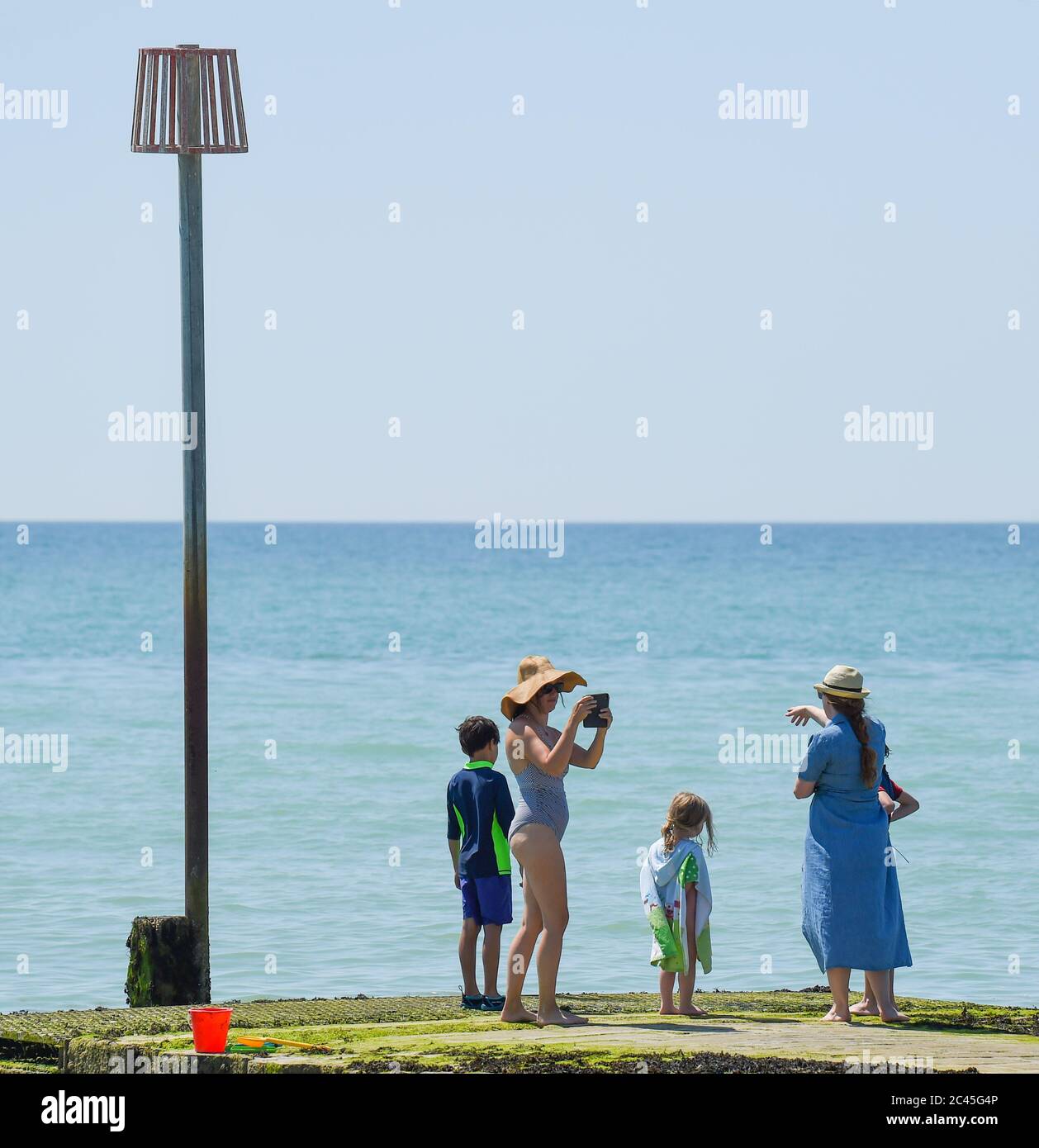 Worthing UK 24th June 2020 - A lady in a large sun hat takes some photographs as crowds hit the beaches at Ferring near Worthing in West Sussex today as they enjoy the heatwave weather  with temperatures reaching 30 degrees in some parts of the South East   : Credit Simon Dack / Alamy Live News Stock Photo