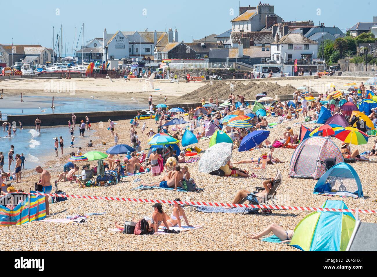 Lyme Regis, Dorset, UK. 24th June, 2020. UK Weather. Beachgoers flock to the seaside resort of Lyme Regis to soak up the scorching hot sunshine on the hottest day of the year only to find the town's main beach closed for major dredging works. Businesses in the town, already suffering major losses from the coronavirus lockdown, could be forgiven for questionning the timing of the works which are taking place on a glorious sunny day just as the town is beignning to welcome visitors back Credit: Celia McMahon/Alamy Live News Stock Photo