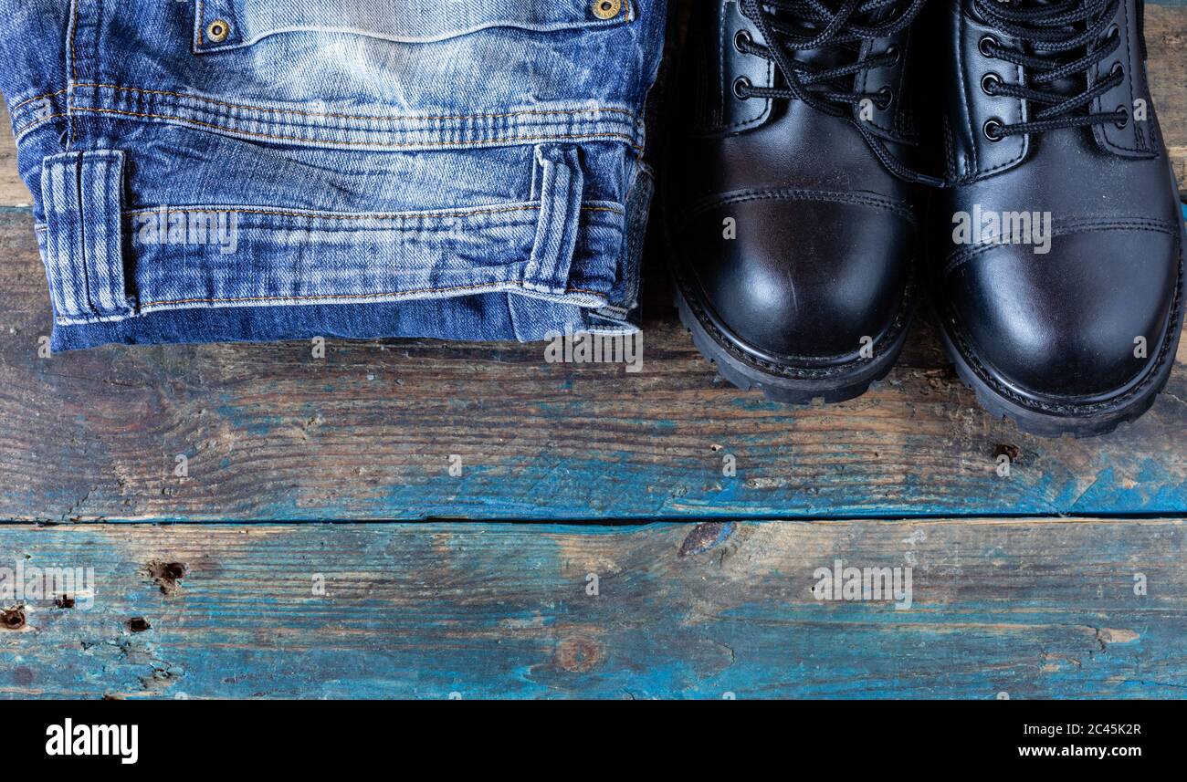 Blue jeans and work boots. Pants on old boards. Black leather shoes. Stock Photo