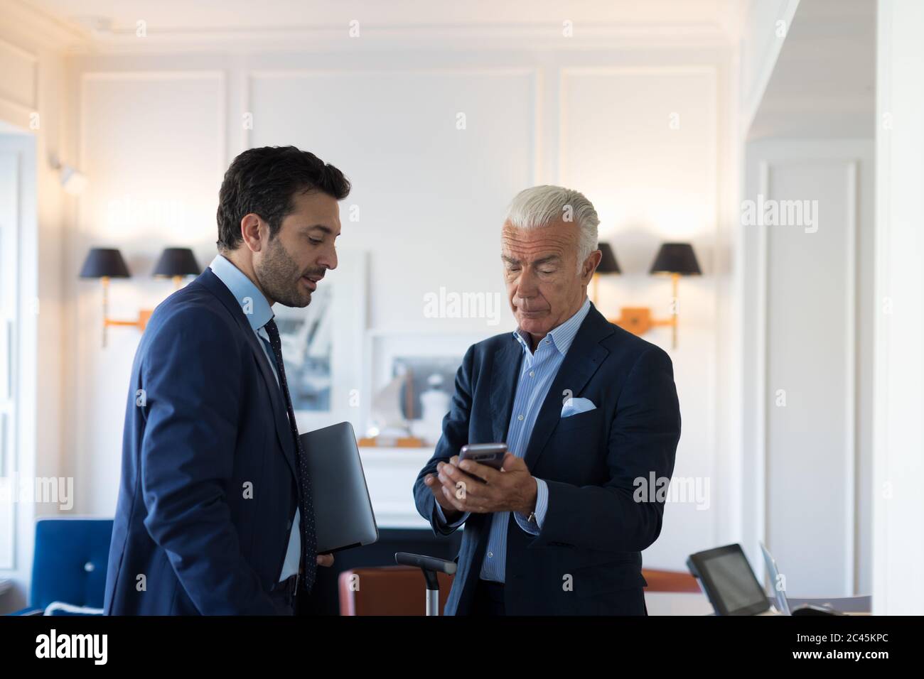 Two businessmen standing indoors, talking Stock Photo - Alamy