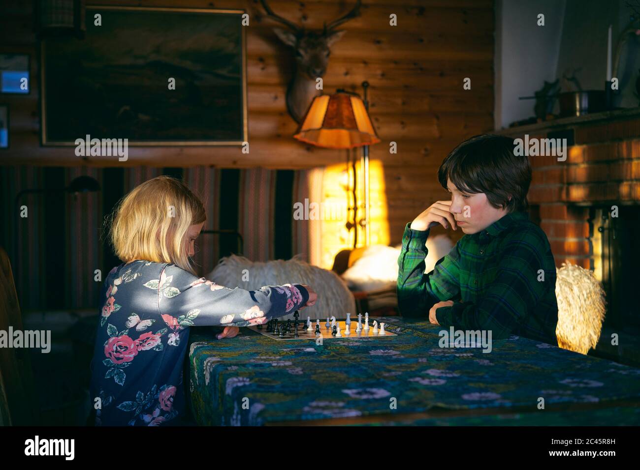 Boy and girl sitting at a table in a log cabin, playing chess, Vasterbottens Lan, Sweden. Stock Photo