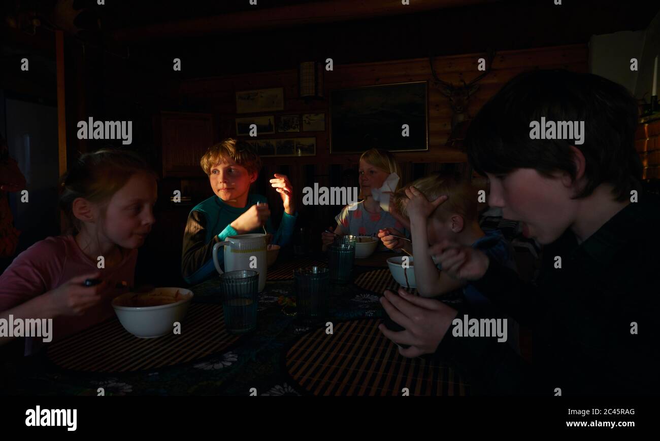 Group of children sitting at a table in a log cabin, eating, Vasterbottens Lan, Sweden. Stock Photo