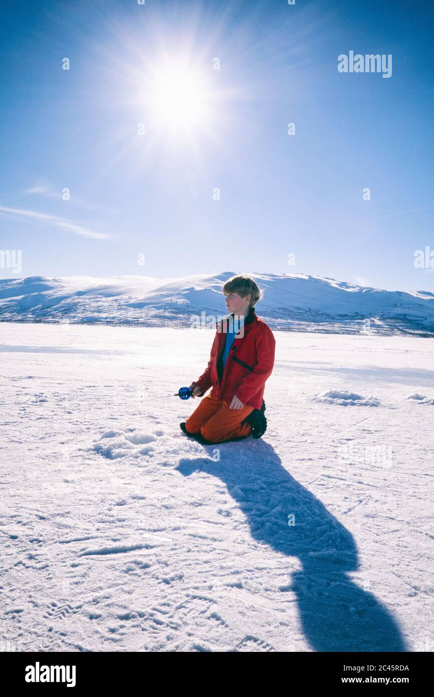 Boy kneeling on frozen lake in Vasterbottens Lan, Sweden. Stock Photo