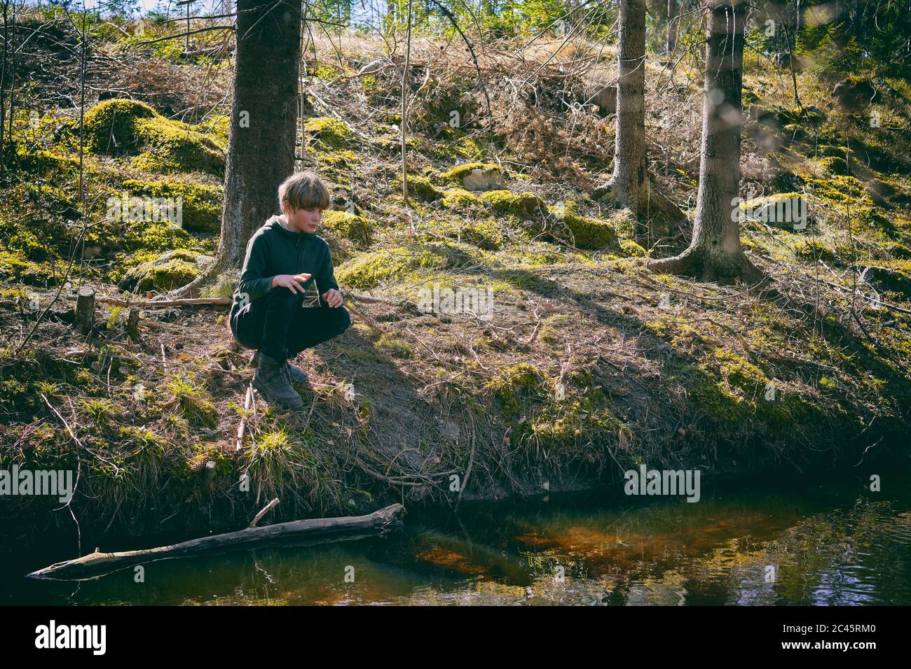 Boy kneeling on riverbank in a forest in Vasterbottens Lan, Sweden. Stock Photo