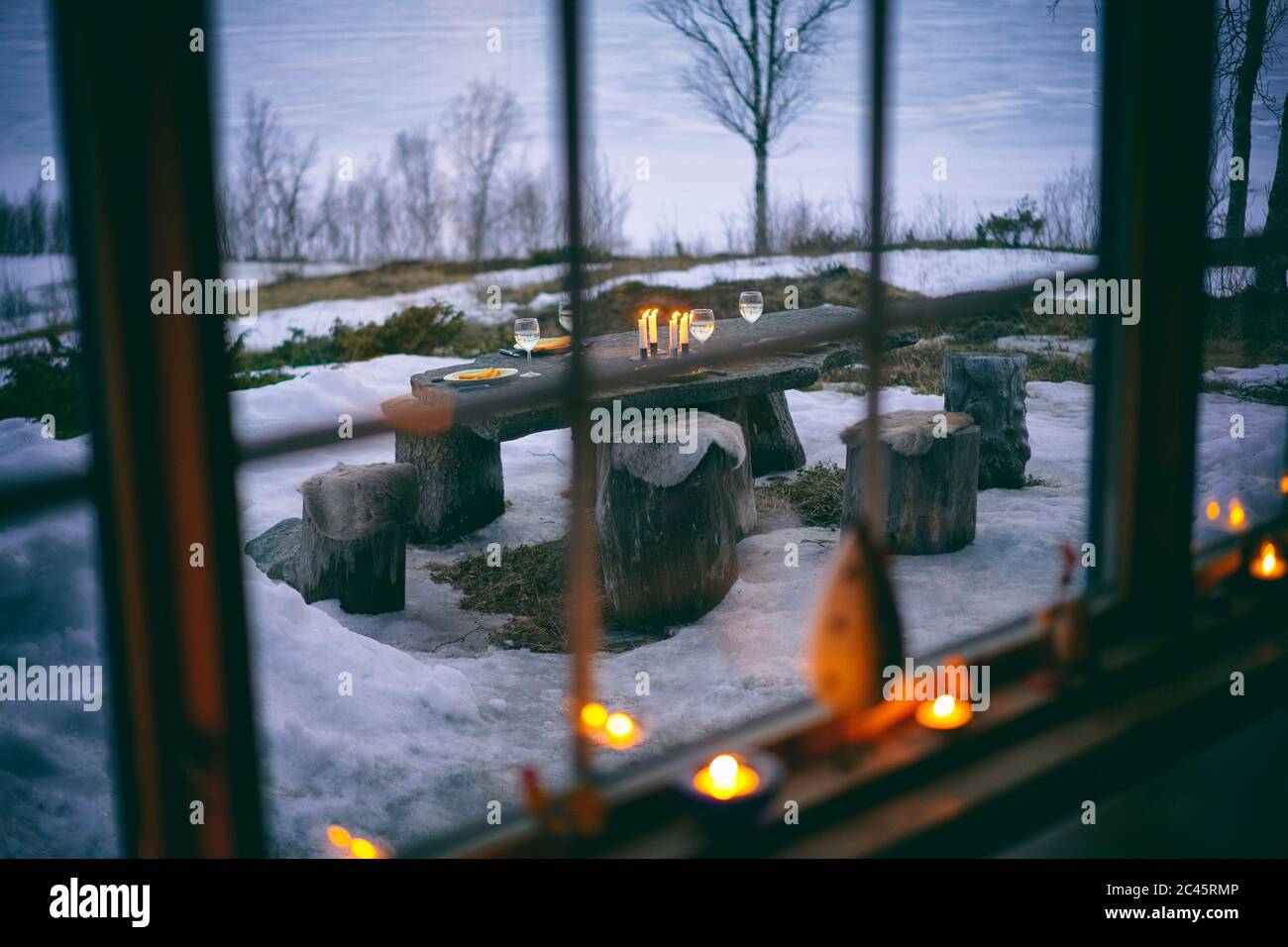 View through log cabin window onto outdoor table set with wine glasses and candles in Vasterbottens Lan, Sweden. Stock Photo