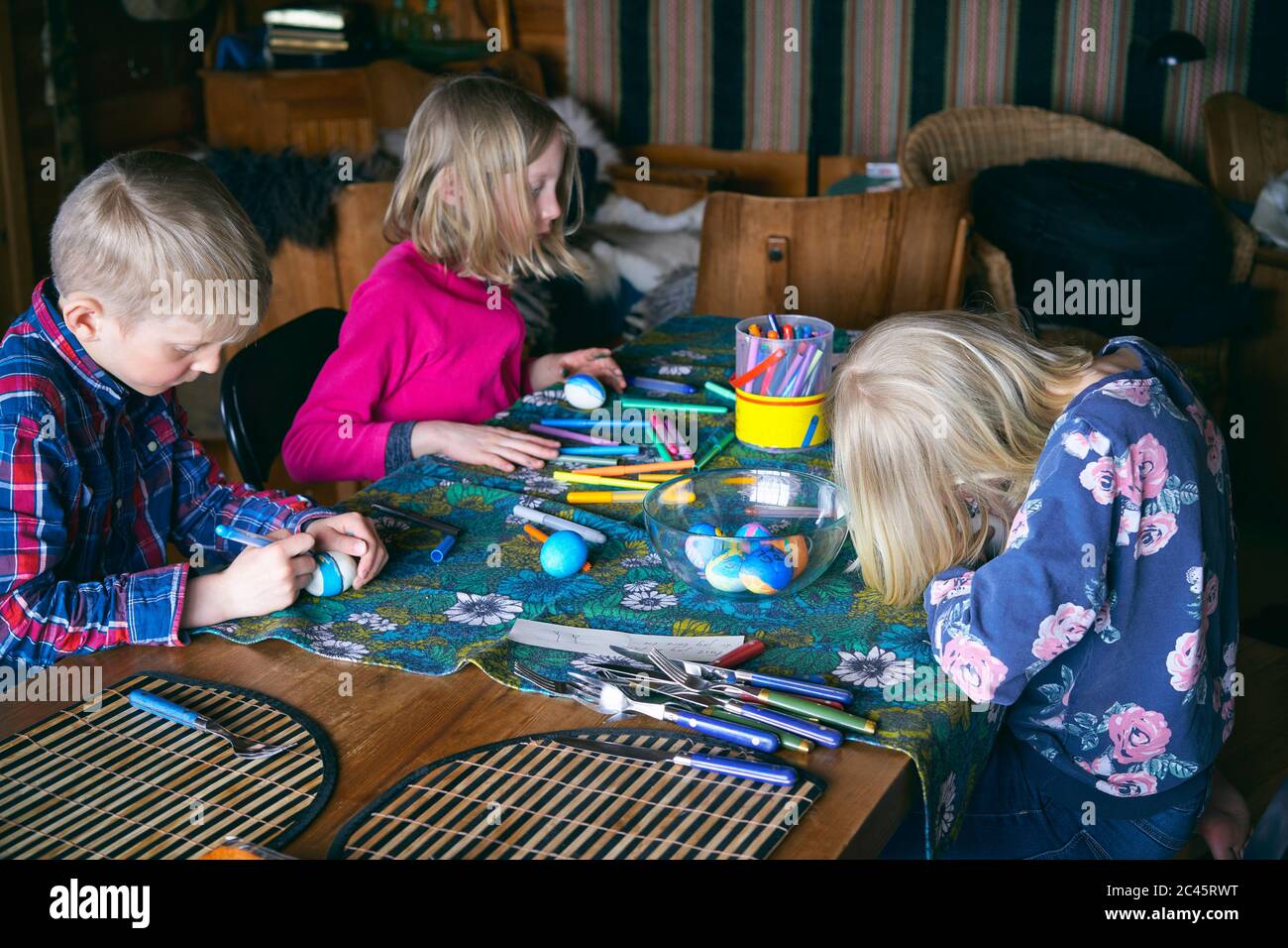 Boy and two girls sitting at a table in a log cabin, doing handicrafts, Vasterbottens Lan, Sweden. Stock Photo