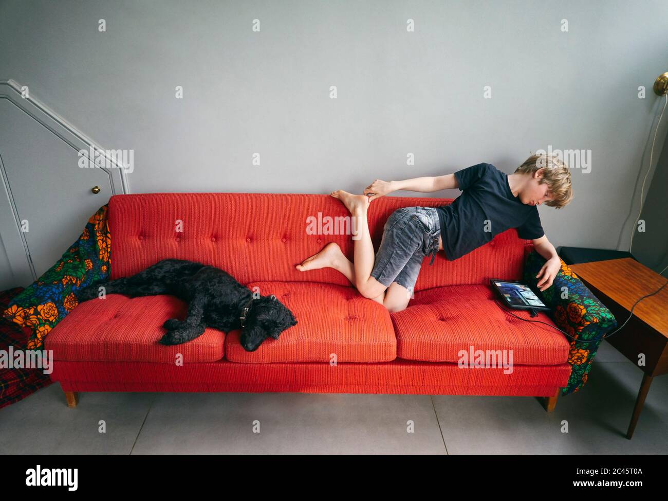 High angle view of boy and black dog lying on red sofa, Vasterbottens Lan, Sweden. Stock Photo
