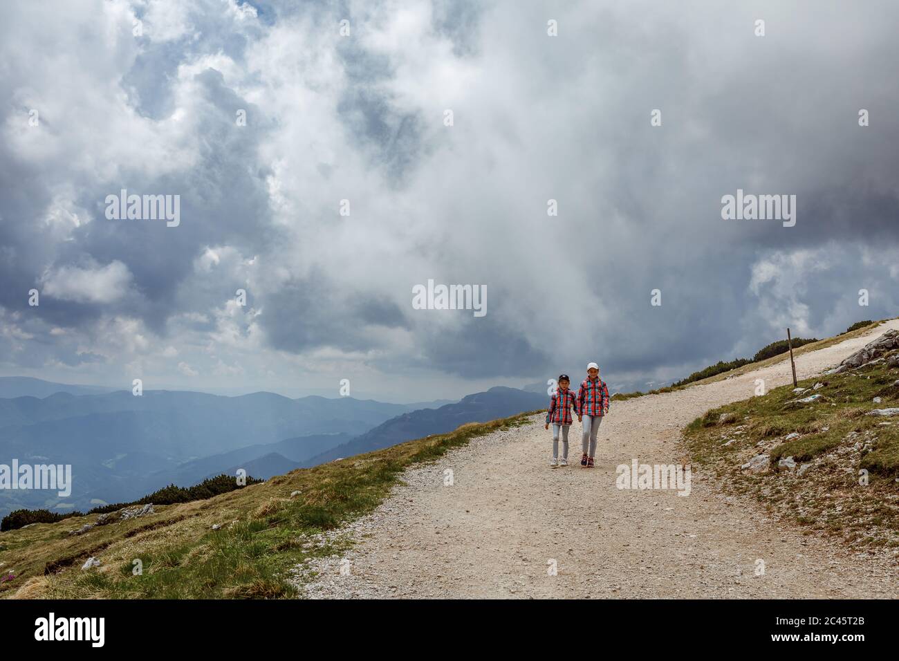 Two young girls walking hand in hand on a mountain path in an alpine ...