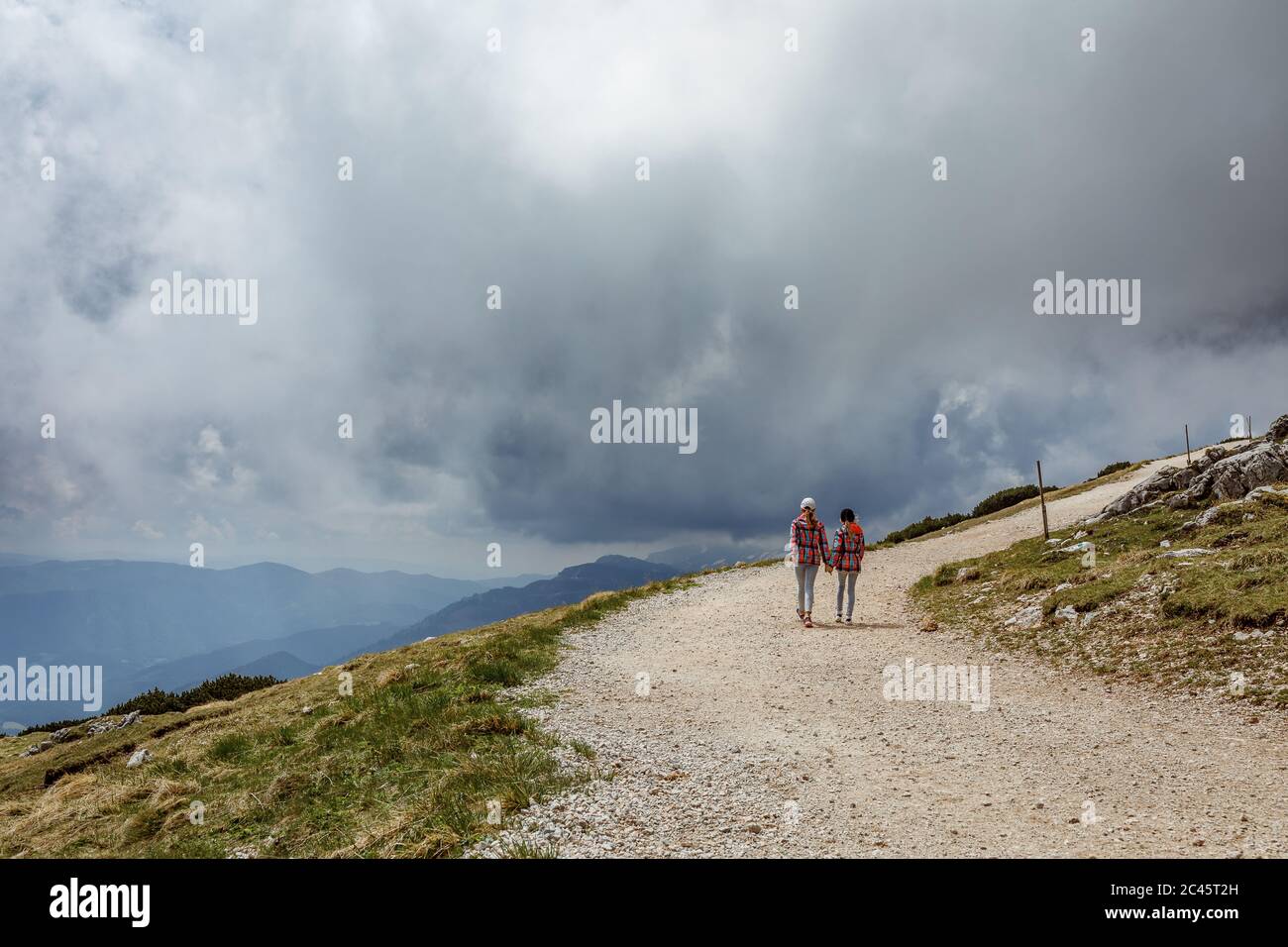 Two young girls walking hand in hand on a mountain path in an alpine ...