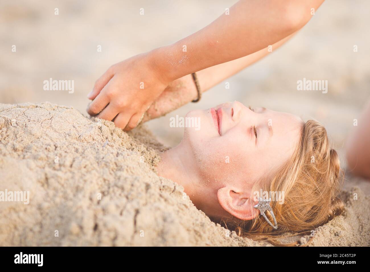 Two hands digging young girl in the sand at the beach Stock Photo