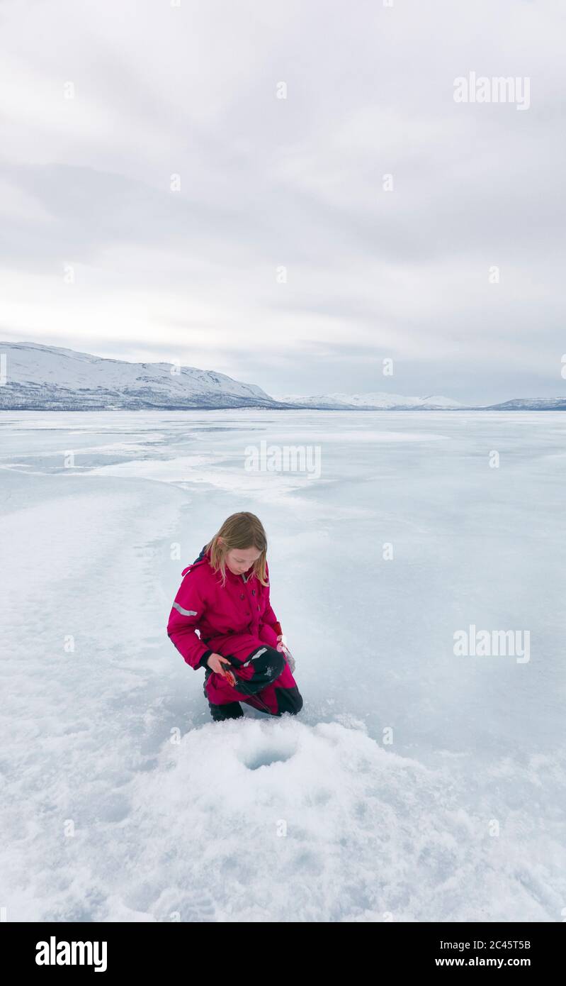 Girl looking at  ice-fishing hole on frozen lake in Vasterbottens Lan, Sweden. Stock Photo