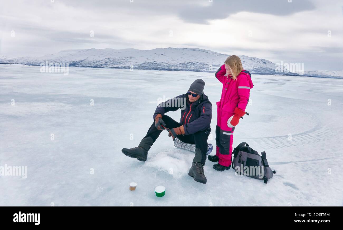 Girl and man ice-fishing on frozen lake in Vasterbottens Lan, Sweden. Stock Photo