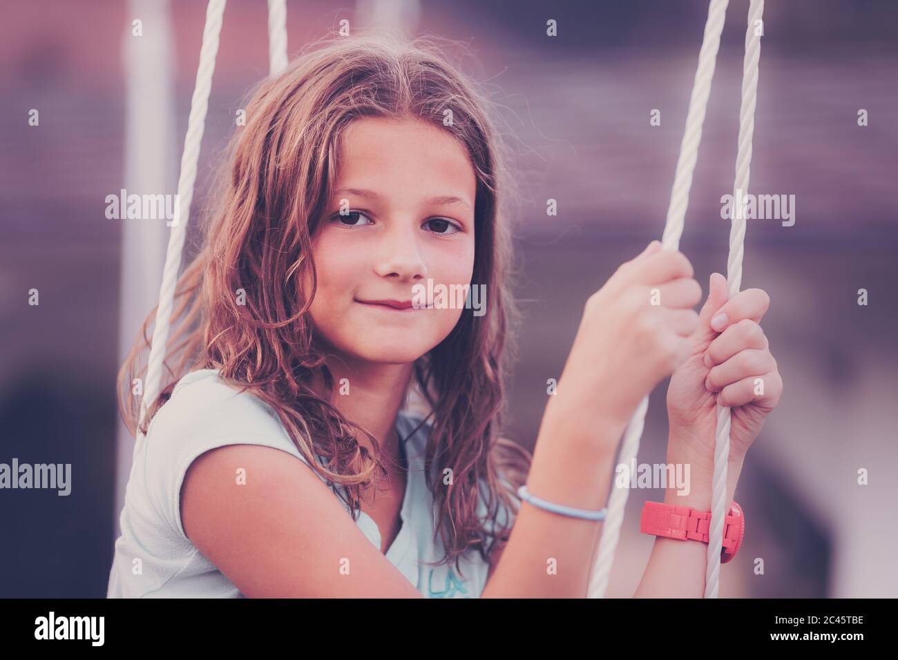 Portrait of young Caucasian girl with brown hair sitting on a swing looking at camera Stock Photo