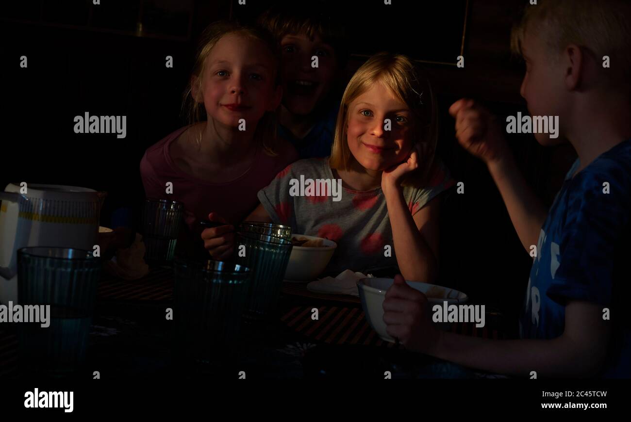 Boy and two girls sitting at a table in a log cabin, eating, Vasterbottens Lan, Sweden. Stock Photo