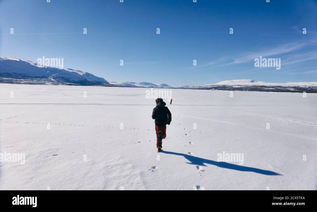 Rear view of two boys running across frozen lake in Vasterbottens Lan, Sweden. Stock Photo