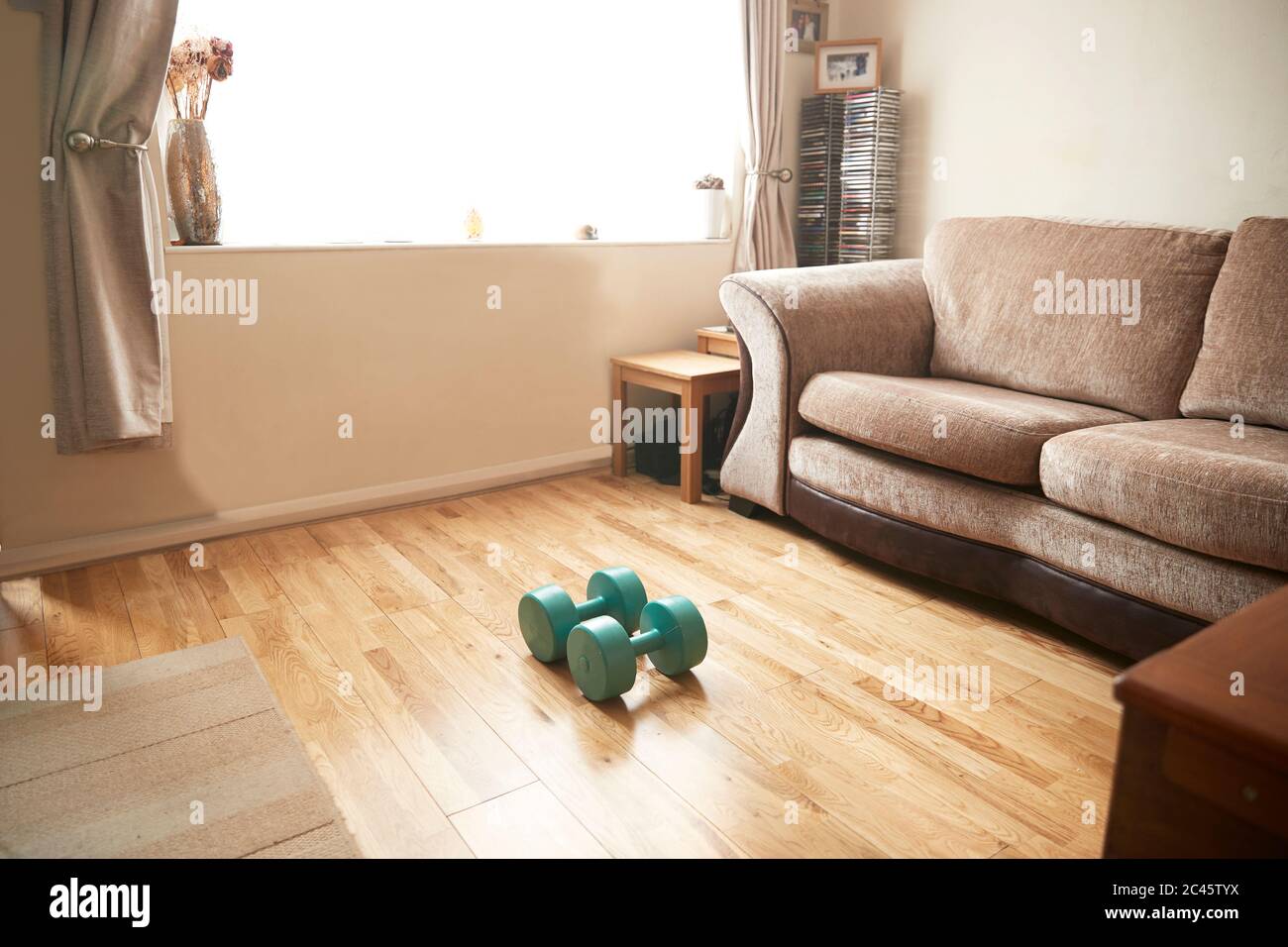 Interior view of living room with turquoise dumbbells lying on wooden floor in front of a brown sofa. Stock Photo