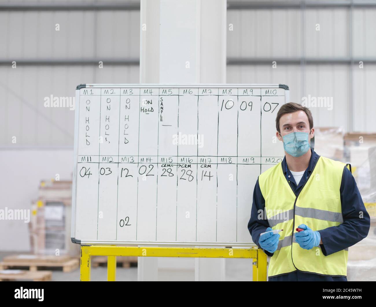 Man wearing surgical face mask and high visibility vest working in a large warehouse. Stock Photo