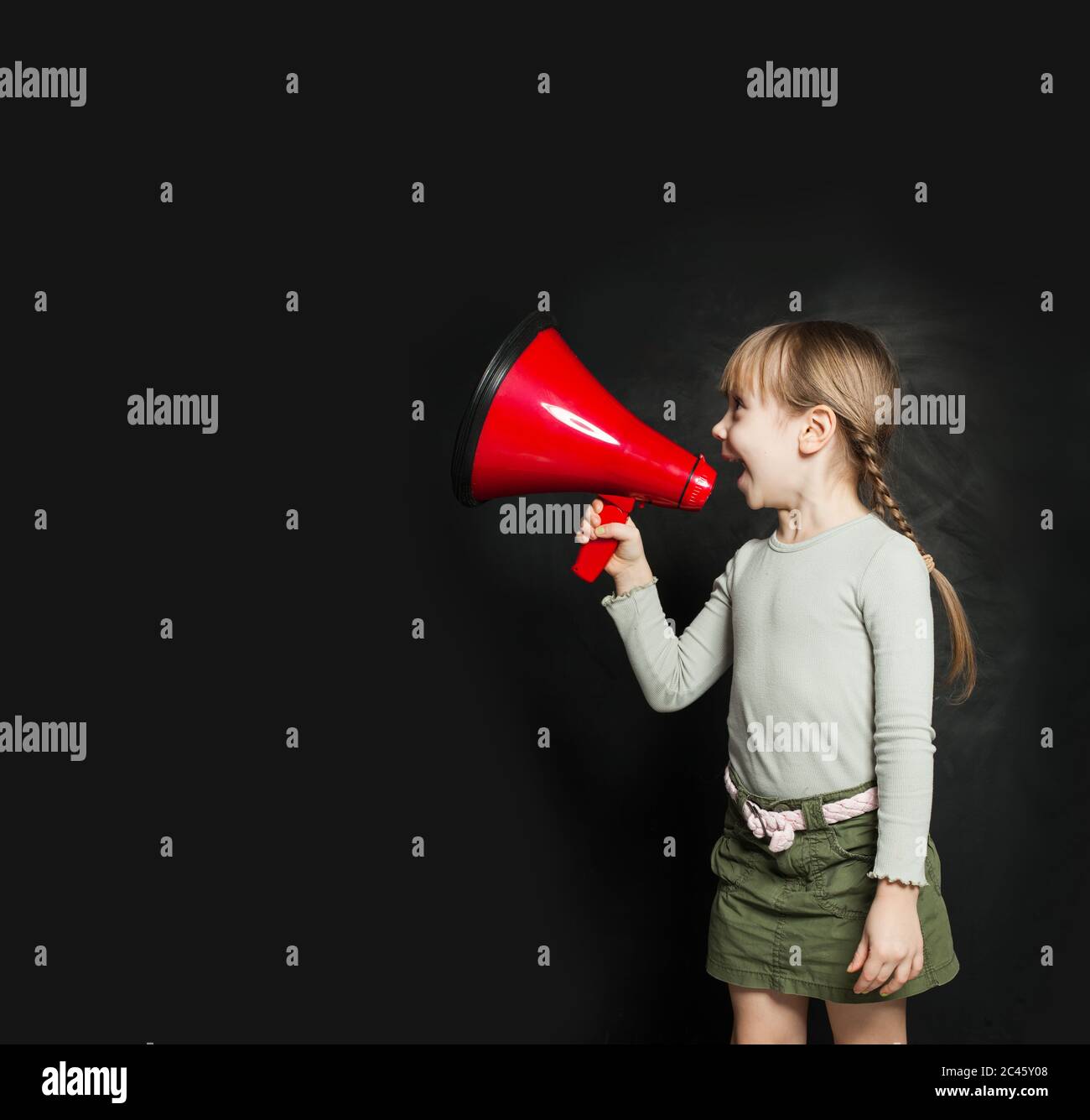 Cute little girl speaking through a megaphone against a blackboard. Kid with loudspeaker Stock Photo