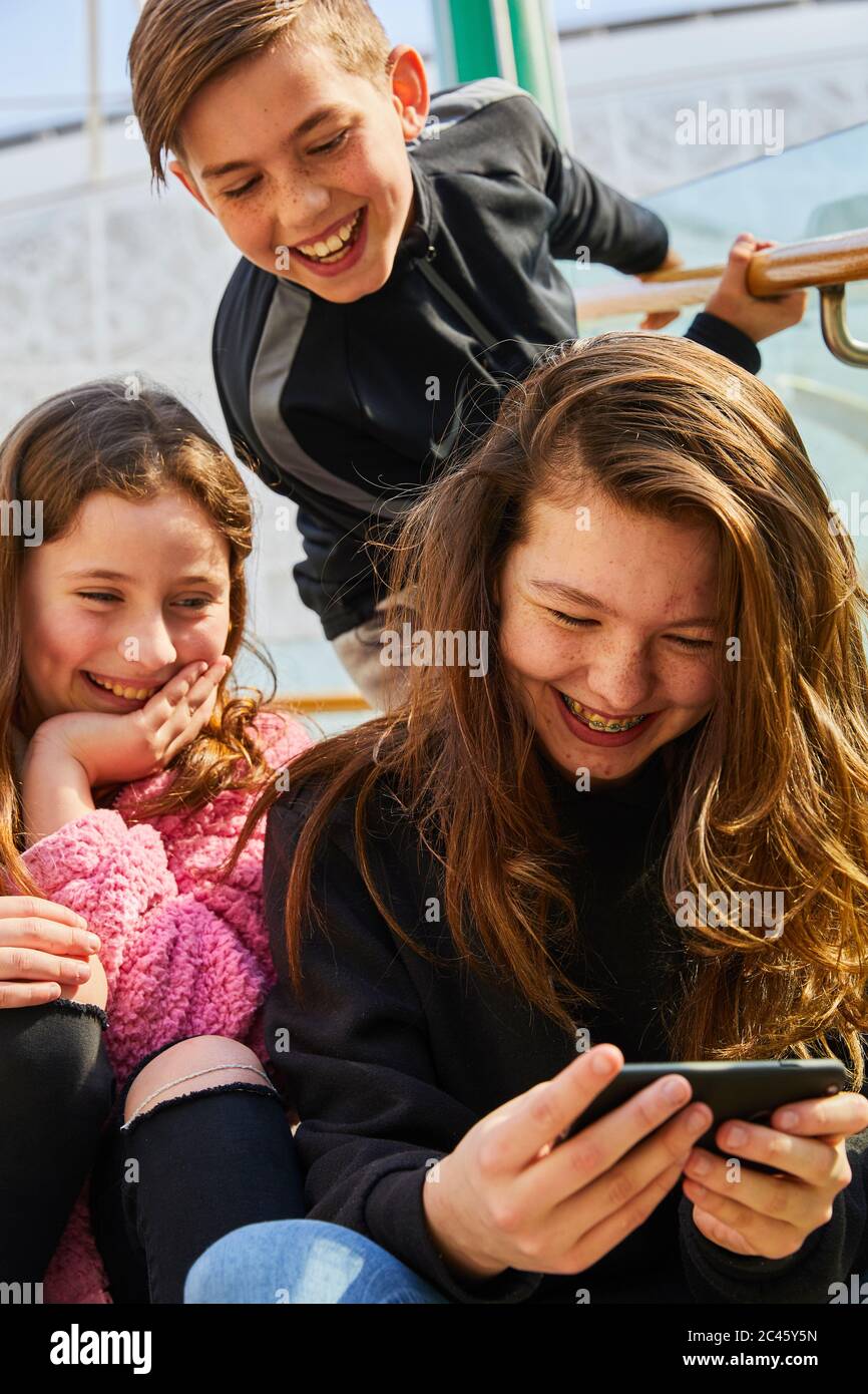 Two teenage girls and boy in a shopping mall, checking their mobile phones. Stock Photo