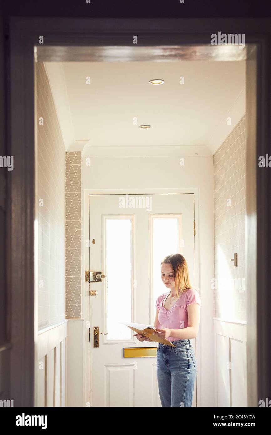 Teenage girl standing in hallway holding large envelope with letter, reading. Stock Photo