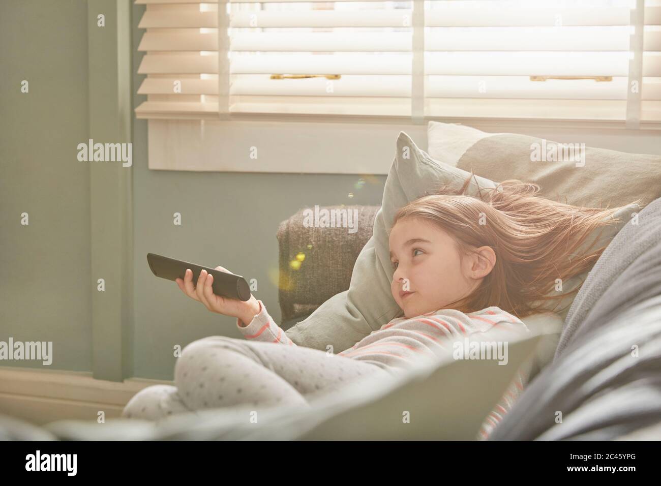 Girl lying on a sofa in her pajamas, watching television. Stock Photo