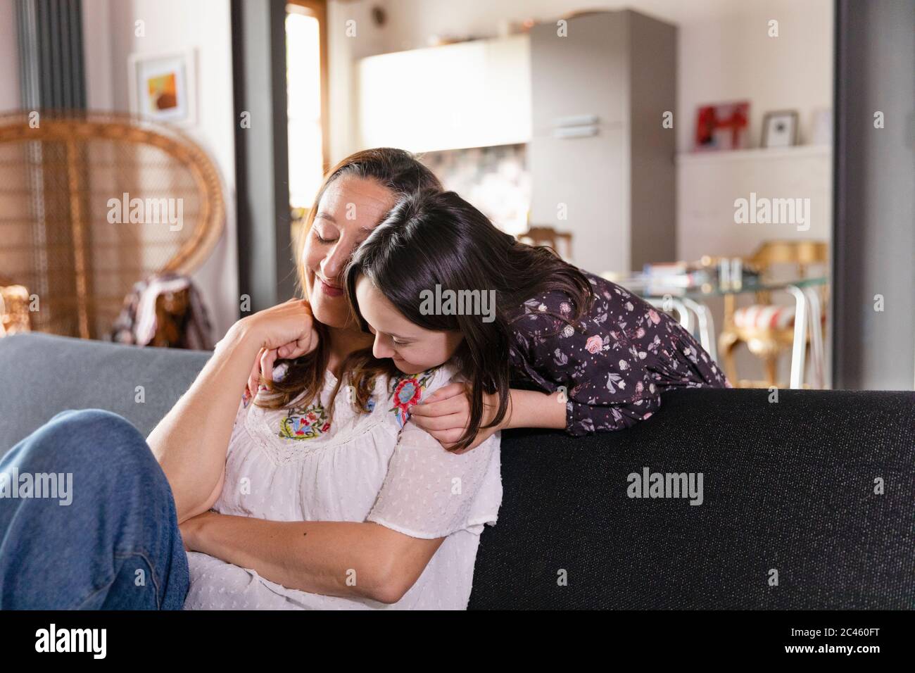 Daughter hugging her mother sitting on living room sofa, during