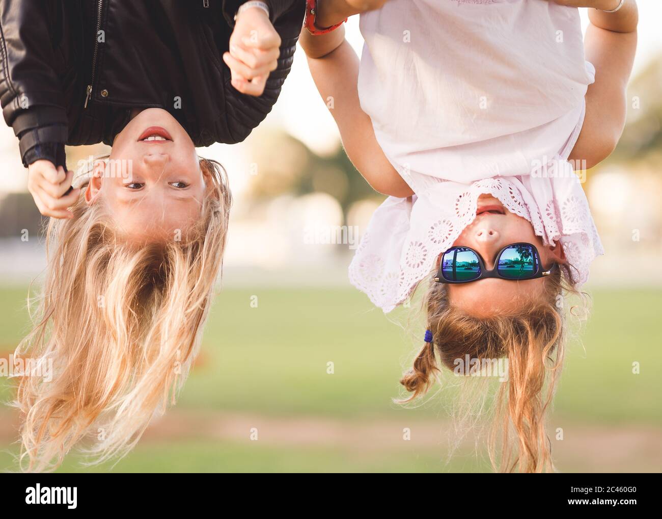 Two young girls, age 8-12, hanging upside down on outdoor fitness device Stock Photo