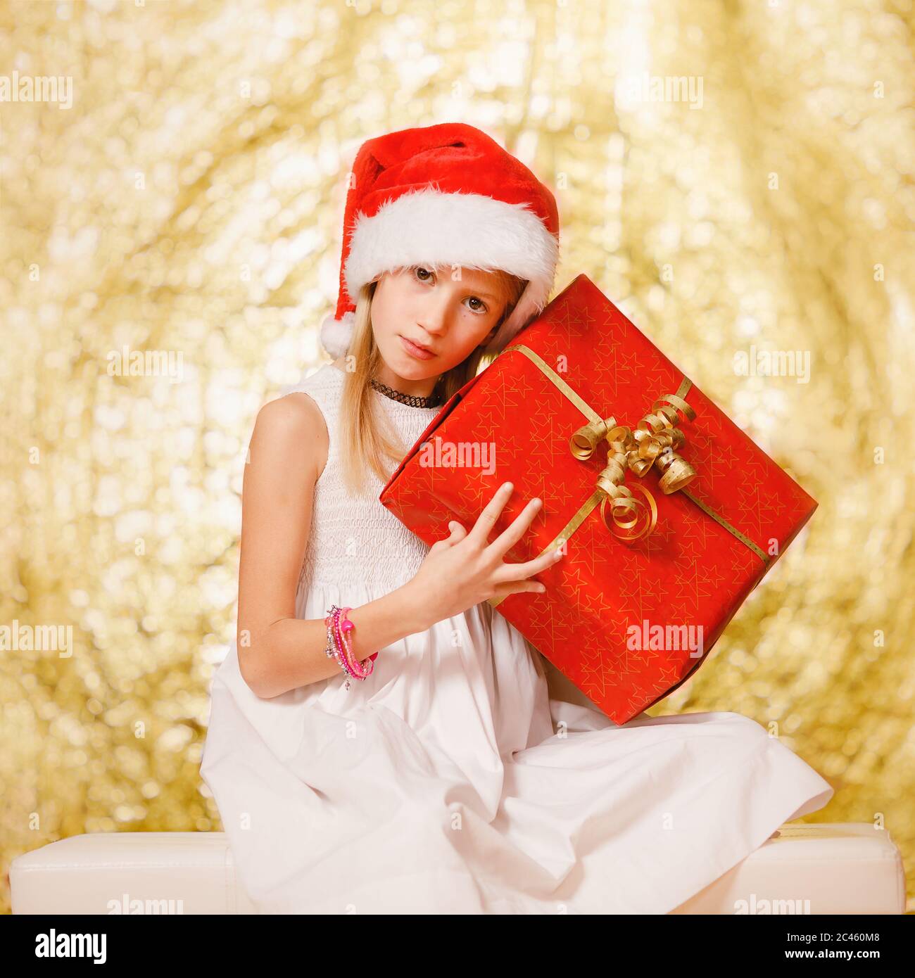Young girl, primary school age, holding Christmas gift, wearing Christmas hat in front of festive Ch Stock Photo